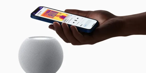 Hand holding an iPhone next to a HomePod mini